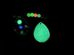 picture showing the beads and front and back of the spinner blade in the dark after having their UV paint and glow beads charged to make them glow. 4 beads glow along with the full back of the blade and the yellow, blue and green dots on the front of the blade.